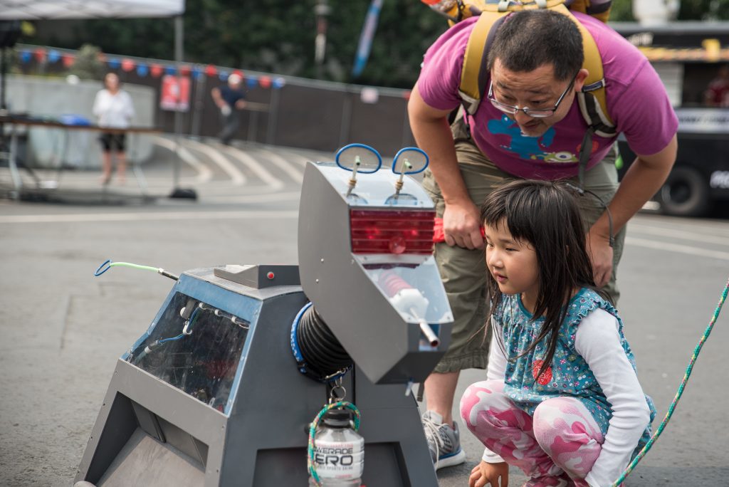 A young girl and her father examine a robot dog art piece.