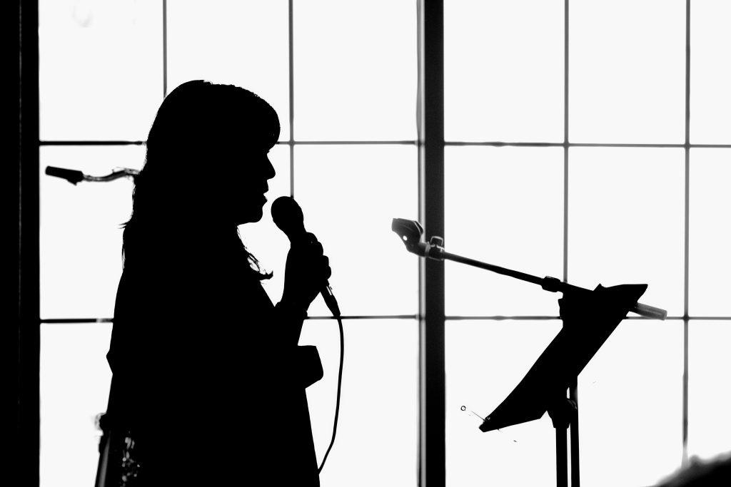 A silhouette of a person holding a microphone to their mouth and a podium in front of them.