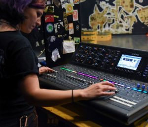 A person in a music studio in front of a mixing board playing with different sounds.