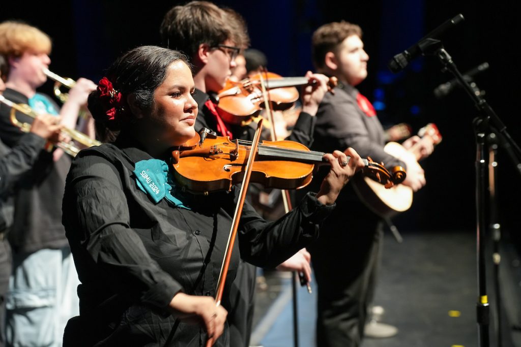 Musicians from the Orquesta Northwest North Seattle Mariachi perform with violins and guitars on a stage.
