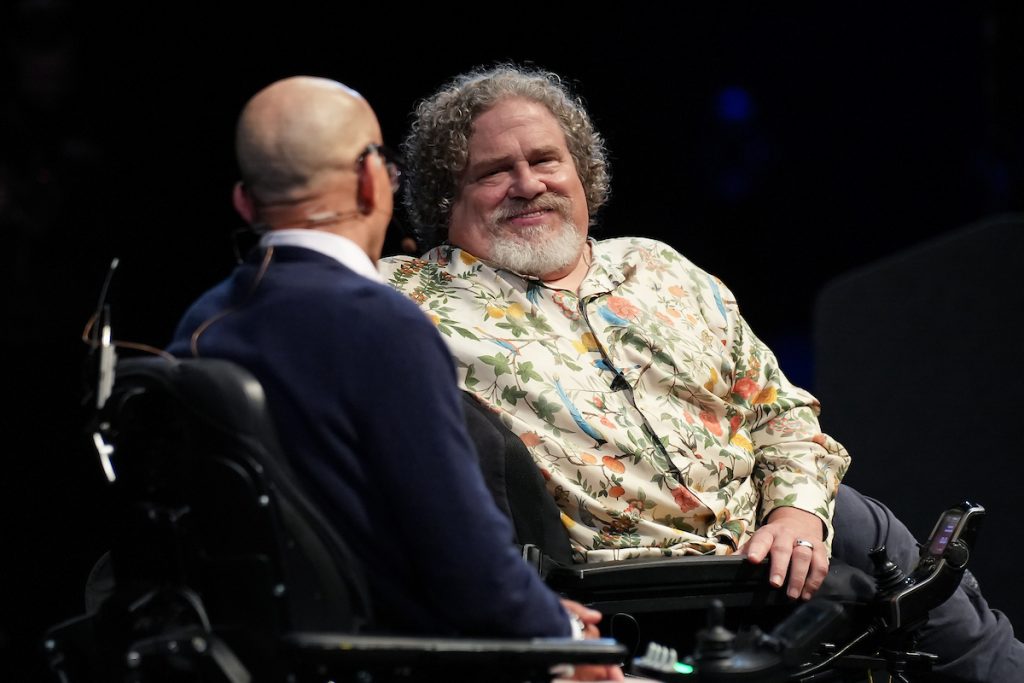 ArtsFund President and CEO Michael Greer and Keynote Speaker Jim LeBrecht sit close together in motorized wheelchairs.