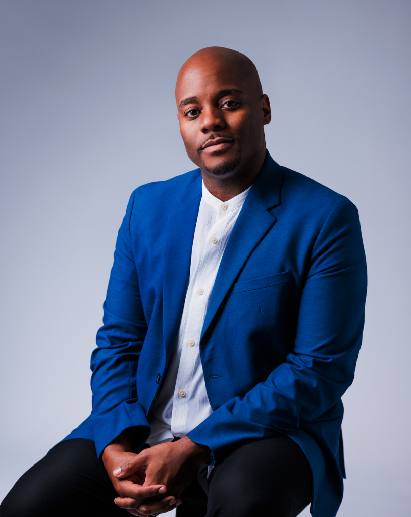 C. Lorenzo Evans III is a bald, Black man wearing a blue blazer over a light-blue, button-up and black slacks.