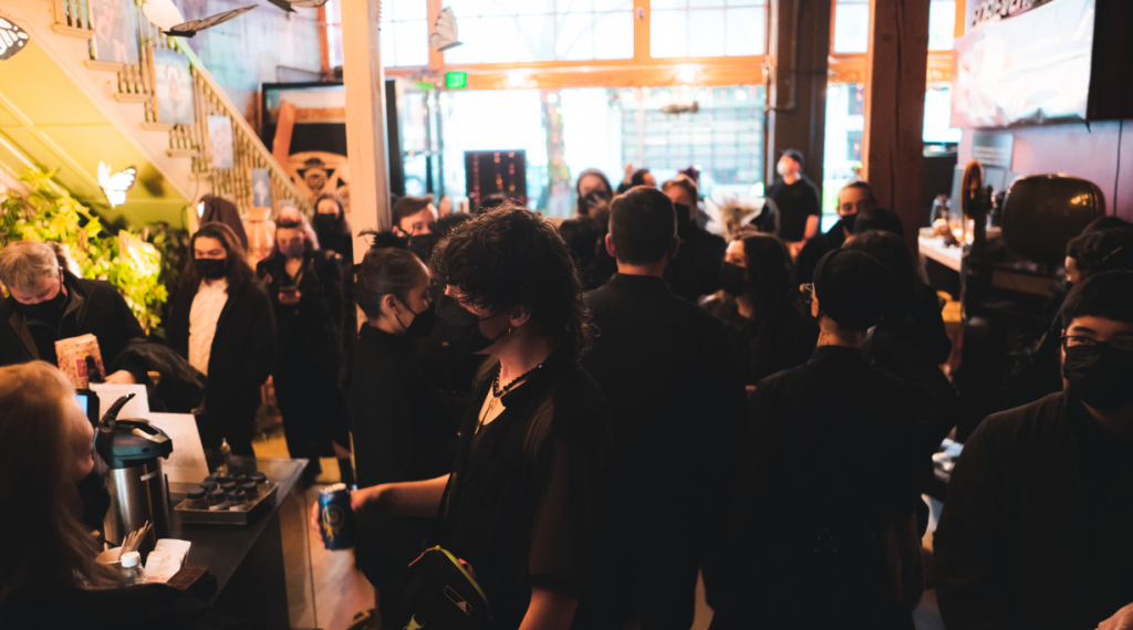 A bunch of filmmakers and writers have gathered in a large space. They're masked and lit by the sunlight from outside.