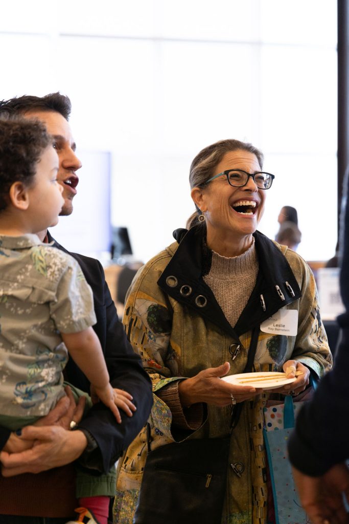 Leslie Ray and an adult man carrying his child talk to an off-screen person.