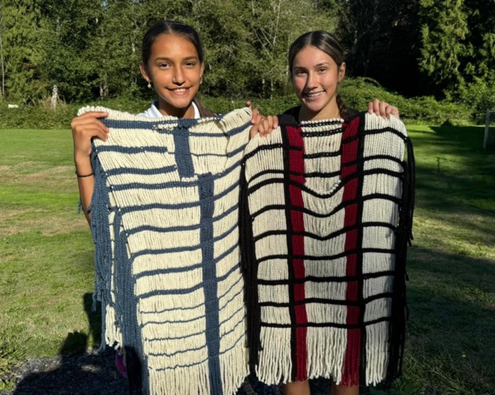 Two youth from Coast Salish Wool Weaving Center are holding up a piece of their work.
