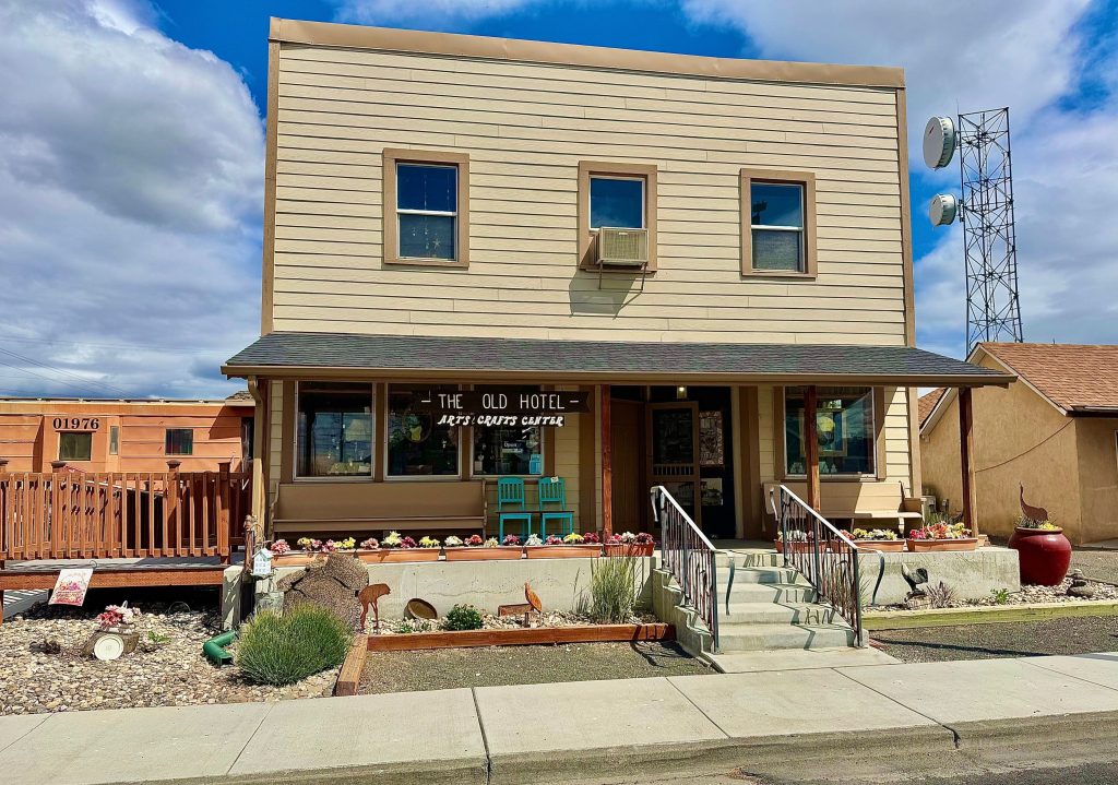 Two-story beige building with a sign reading 'The Old Hotel Arts & Gifts Center' and a small front porch with stairs.