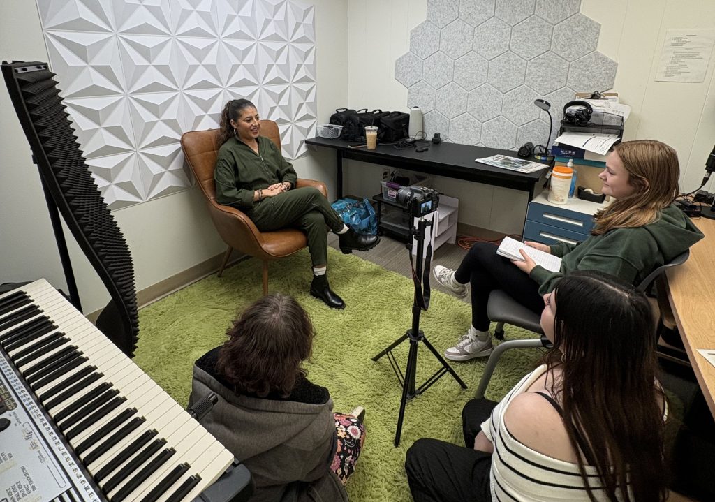 Three people conducting an interview or discussion in a small soundproof room with acoustic panels and recording equipment.
