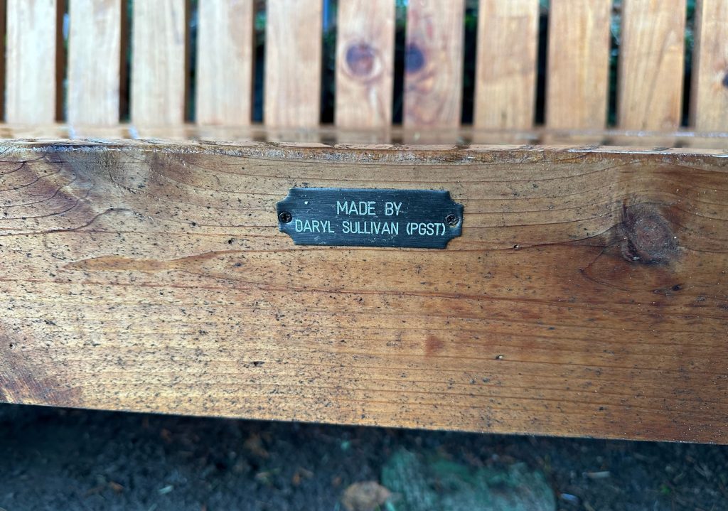 Close-up of a wooden bench with a metal plaque reading 'Made by Daryl Sullivan (Post)'.