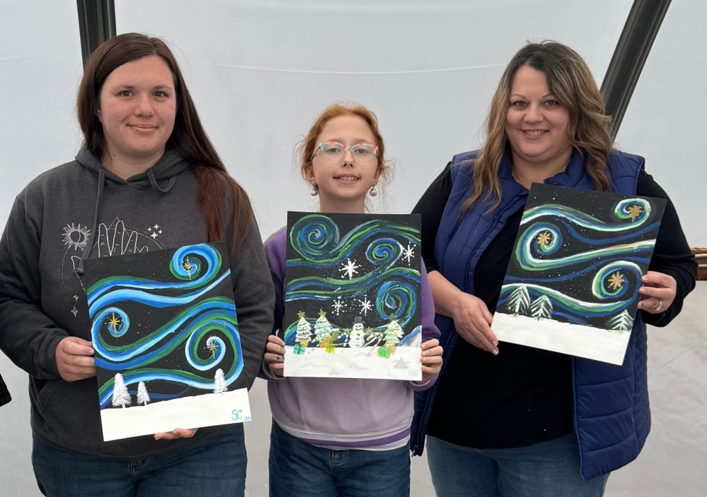Three people holding paintings of swirling night skies with stars and snowy landscapes featuring pine trees.