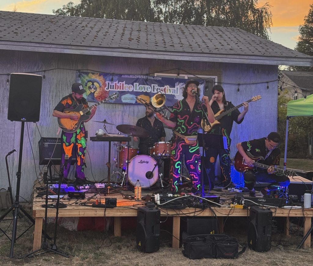Band performing on an outdoor wooden stage at sunset with colorful outfits and musical instruments.